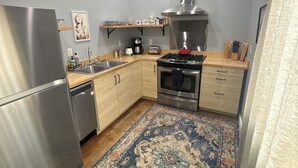 Eine kompakte Küche mit einem Edelstahlkühlschrank, einem Gasherd und einem eingebauten Backofen. Es gibt eine Holz Arbeitsplatte und einen gemusterten Teppich auf dem Boden.