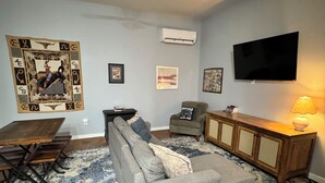 Ein Wohnzimmer mit grauem Sofa, einem gemusterten Teppich, einem Deckenventilator, einem Flachbildfernseher und einer Holzkabine.