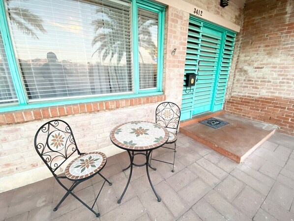 An outdoor seating area with two metal chairs and a round table, a blue door, and a brick wall.