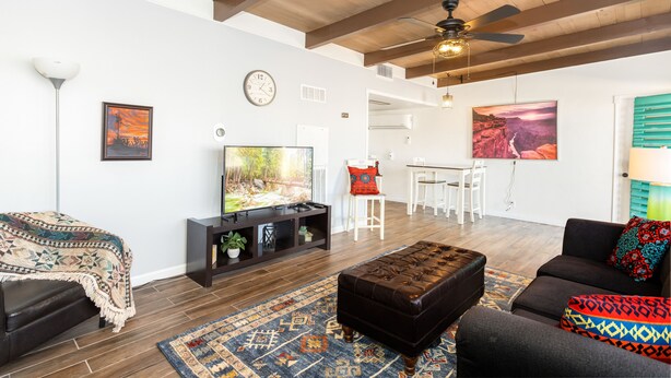 A living room with a TV, sofa, ottoman, and a dining area with chairs and a table. - The Teal Door | UofA Central Newly Renovated 1BR (Tucson)