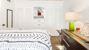 A bedroom with a bed, a dresser, a mirror, and a window with shutters. - The Teal Door | UofA Central Newly Renovated 1BR (Tucson)