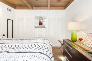Ein Schlafzimmer mit einem Bett, einem Schminktisch, einem Spiegel und einem Fenster mit Rollläden.