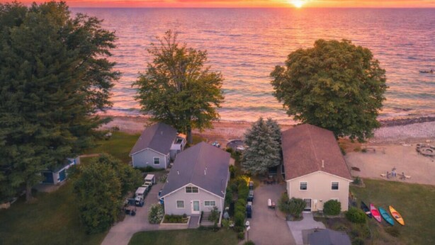 An aerial view of a coastal residential area with houses, trees, and a beach.