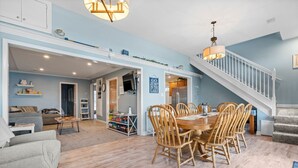 A spacious living area with a dining table and chairs, a staircase, and a kitchen in the background.