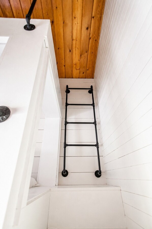 A narrow stairway with a black metal ladder, white walls, and wooden ceiling. - Ainsley's Cove - Swim spa open all year! (Port Sanilac)