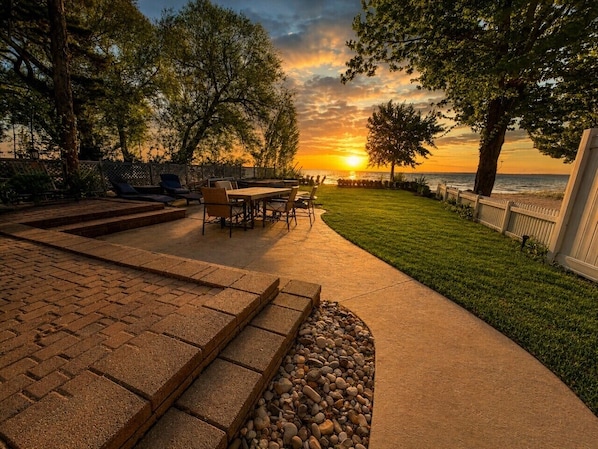A patio with outdoor furniture, a paved walkway, and a view of the sunset over the water.