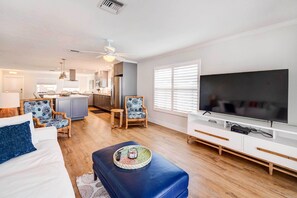 Relax in this stylish living room with a large flat-screen TV, comfortable seating, and a kitchen area.