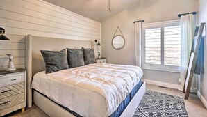 Un dormitorio con cama, mesita de noche, cómoda, ventilador de techo, ventana con cortinas y espejo montado en la pared.