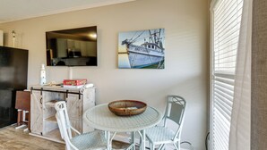 A dining area with a round table, white chairs, a basket, and a painting of a boat on the wall. - On-Site Beach Access: Apt in Hilton Head Island! (Hilton Head Island)