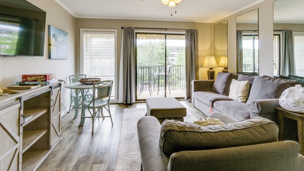 A living room with a sofa, ottoman, and a ceiling fan. There is a dining table with chairs and a TV mounted on the wall. - On-Site Beach Access: Apt in Hilton Head Island! (Hilton Head Island)