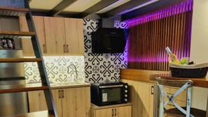Una cocina compacta con armarios de madera, microondas, lavamanos y un taburete pequeño.
