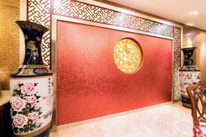A room with a red textured wall, a decorative circular window, and traditional vases. - Yu Jing Lou Hotel (Ci County)