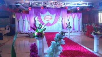 Un escenario con alfombra roja, arreglos florales y un fondo con la palabra 'Wedding'.