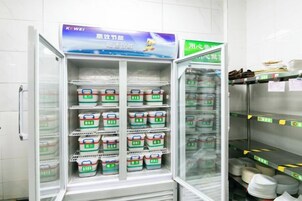A commercial refrigerator stocked with food items, a freezer compartment, and a shelf with plates and utensils.