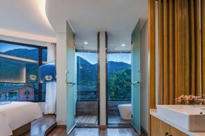 Una habitación de hotel moderna con una cama grande, un baño con lavabo y vistas a las montañas.