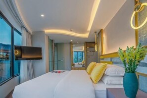 Habitación de hotel moderna con una cama grande, una mesita de noche, un televisor y vistas a la ciudad.