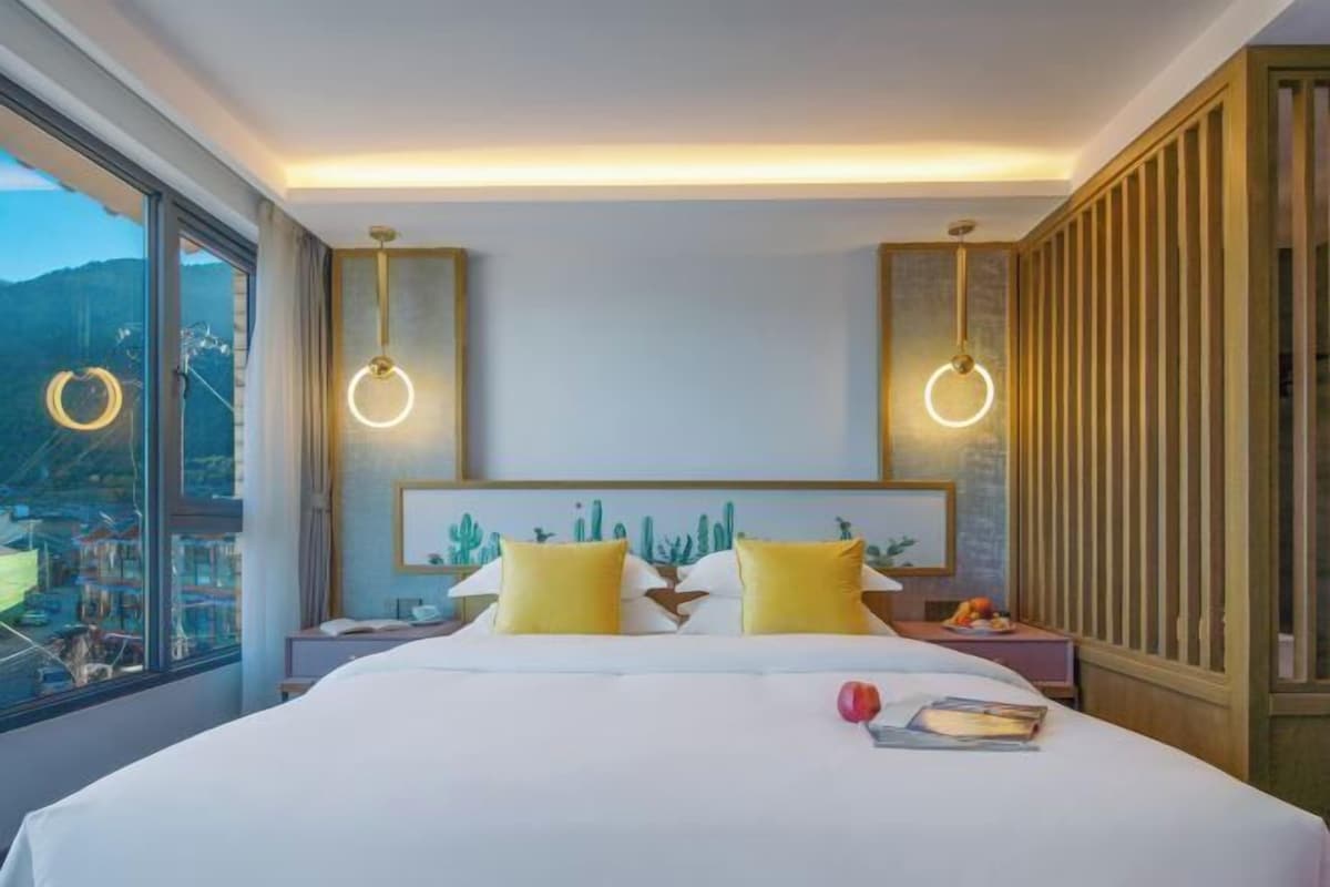 A hotel room with a large bed, two bedside tables, a window with a view, and a headboard with a cactus design.