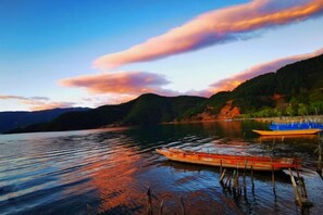 Un lago tranquilo con barcos, un muelle y montañas al fondo.