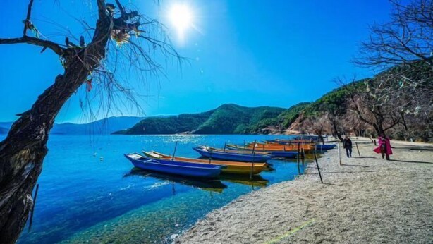 A beach with boats, clear water, and a hilly landscape. - Lugu Lake Yueji Hotel (Ninglang)