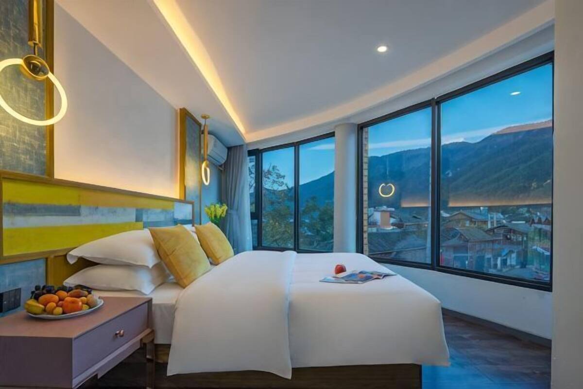 Una habitación de hotel moderna con una cama grande, una mesita de noche y vistas a un paisaje montañoso.