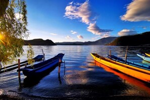 A calm lake with boats docked on the shore, surrounded by hills.