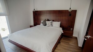 A bedroom with a wooden headboard, a large bed with white bedding, two bedside tables, and a window with a view. - Modern apartment, 5 min from the central park! (Quezaltenango)