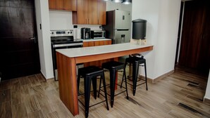 A modern kitchen with wooden cabinets, a stainless steel refrigerator, a built-in oven, a coffee maker, and a black trash can. - Modern apartment, 5 min from the central park! (Quezaltenango)