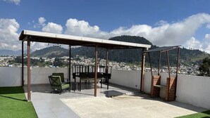 A rooftop patio with a pergola, seating, and a view of a city and mountains. - Modern apartment, 5 min from the central park! (Quezaltenango)
