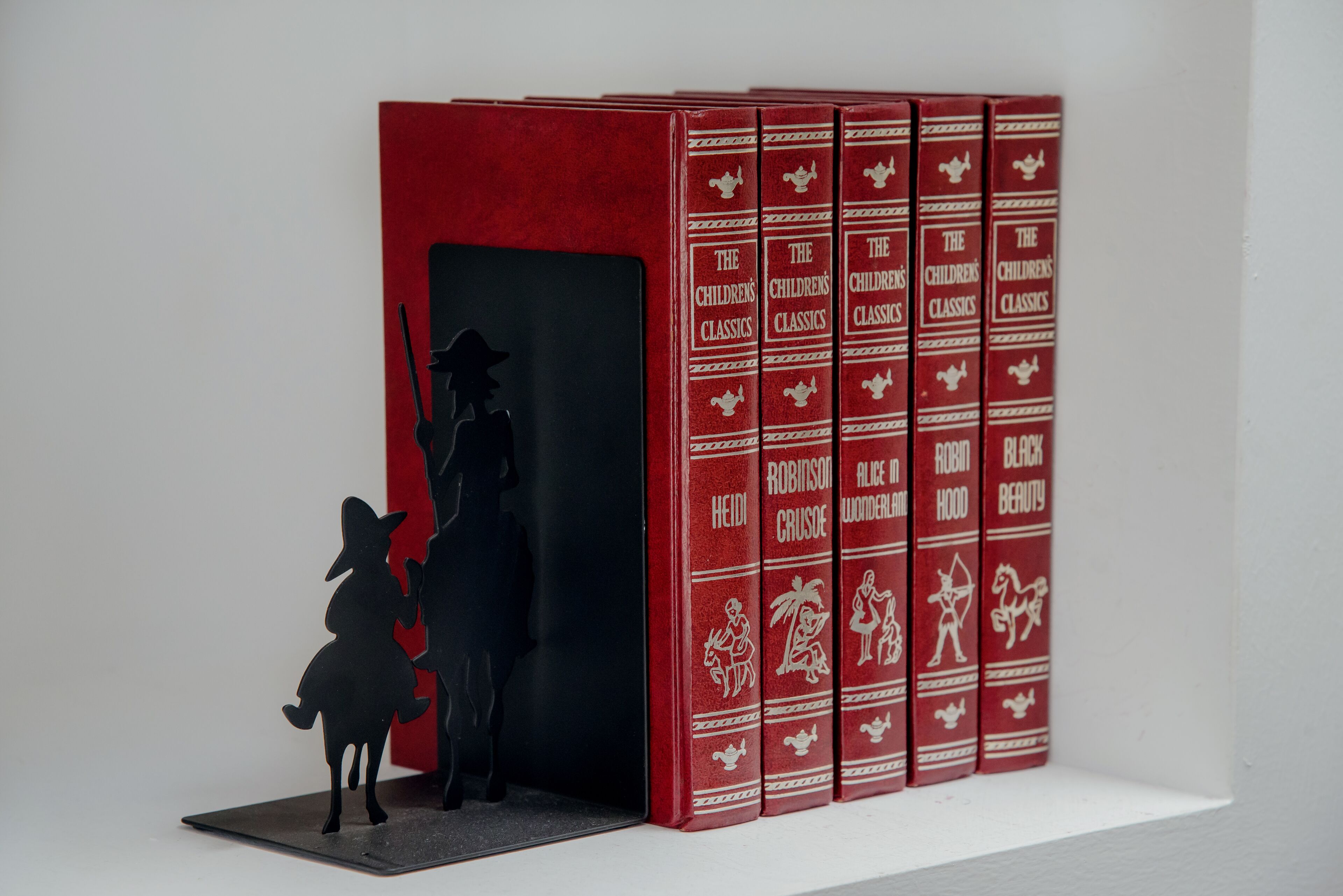 Une collection de livres à couverture rouge intitulée « Les classiques de la littérature enfantine », dont les couvertures présentent des silhouettes de personnages.