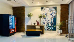 Een moderne lobby met een automaat, een centraal zithoek en een groot abstract schilderij aan de muur.