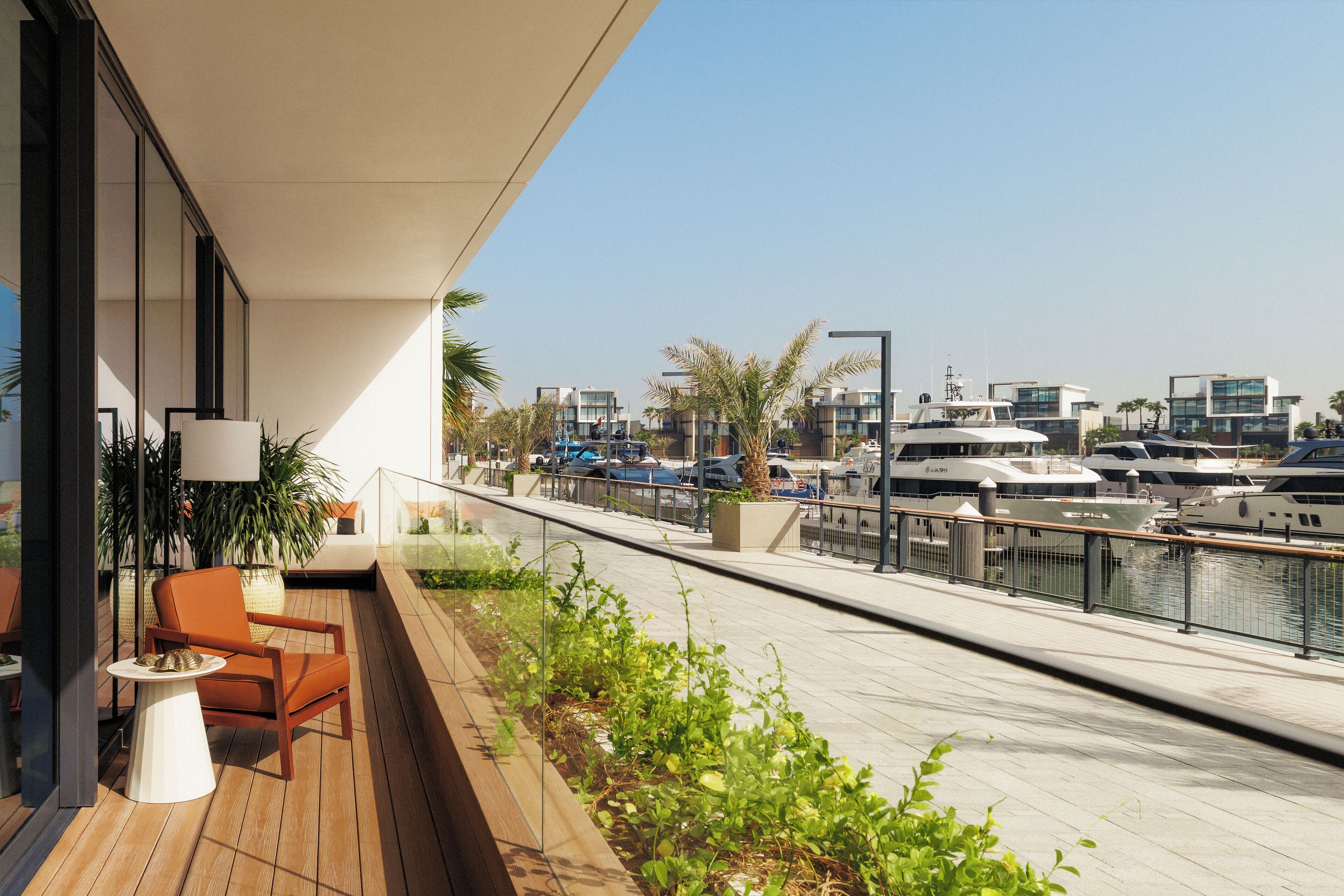 Una terraza moderna al aire libre con piso de madera, una mesa blanca y una silla naranja. Al fondo, varios barcos amarrados en un puerto deportivo con edificios modernos y palmeras.
