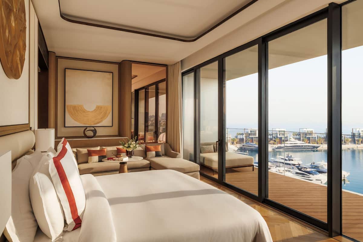 A modern hotel room with a large bed, a sofa, and a view of a marina with boats.