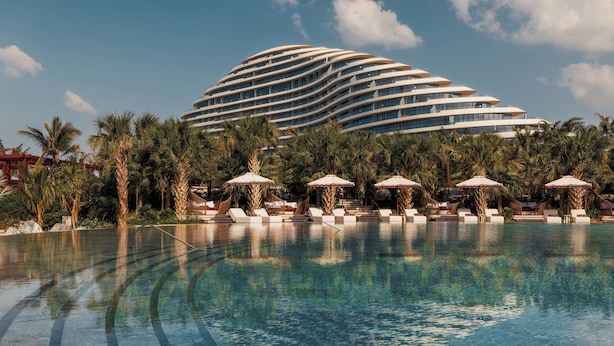 A modern hotel with a unique curved architecture, a pool area with lounge chairs and umbrellas, and palm trees. - Jumeirah Marsa Al Arab Dubai (Dubai)