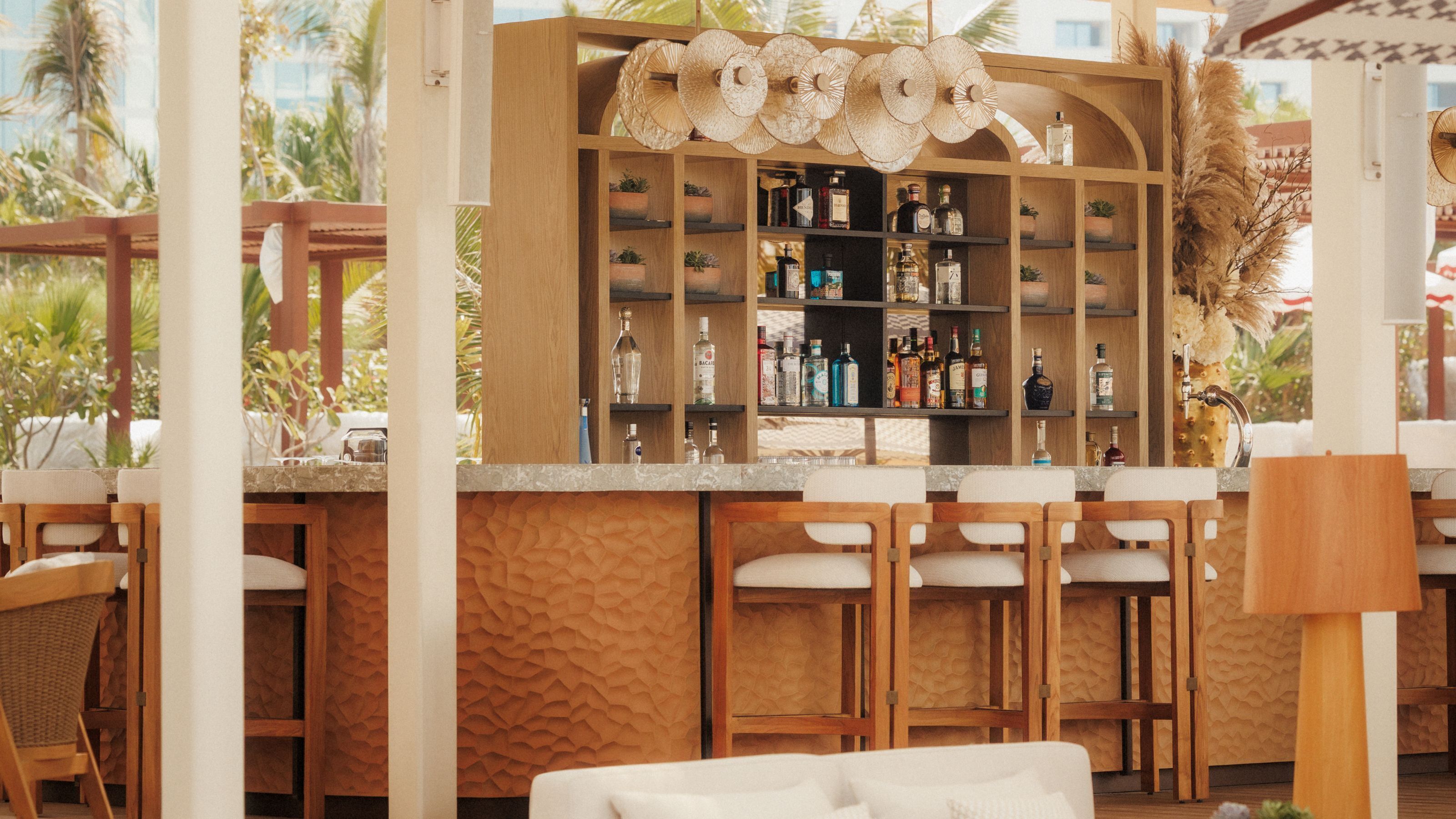 Zona de bar con estantes de madera, sillas y vistas tropicales.