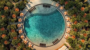 An aerial view of a resort with a circular pool surrounded by palm trees and sun loungers.