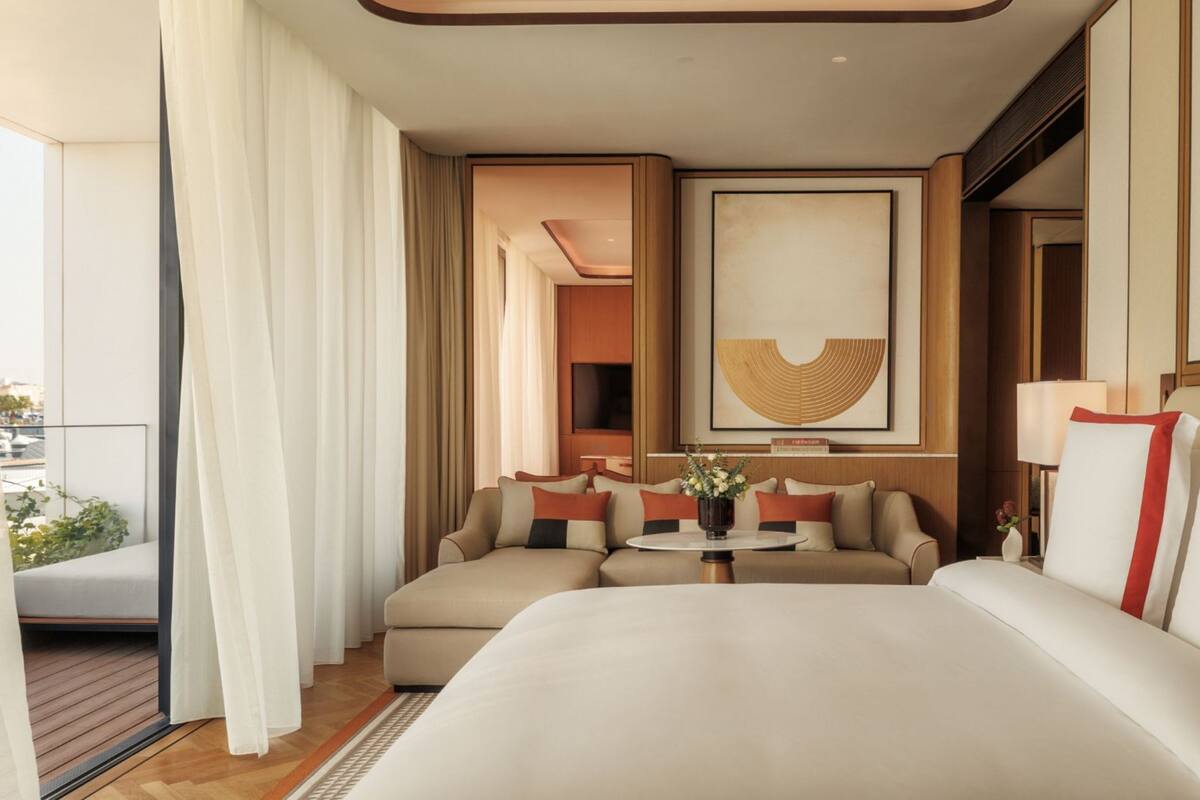 A hotel room with a large bed, a sofa, a small table with a vase, and a painting on the wall.