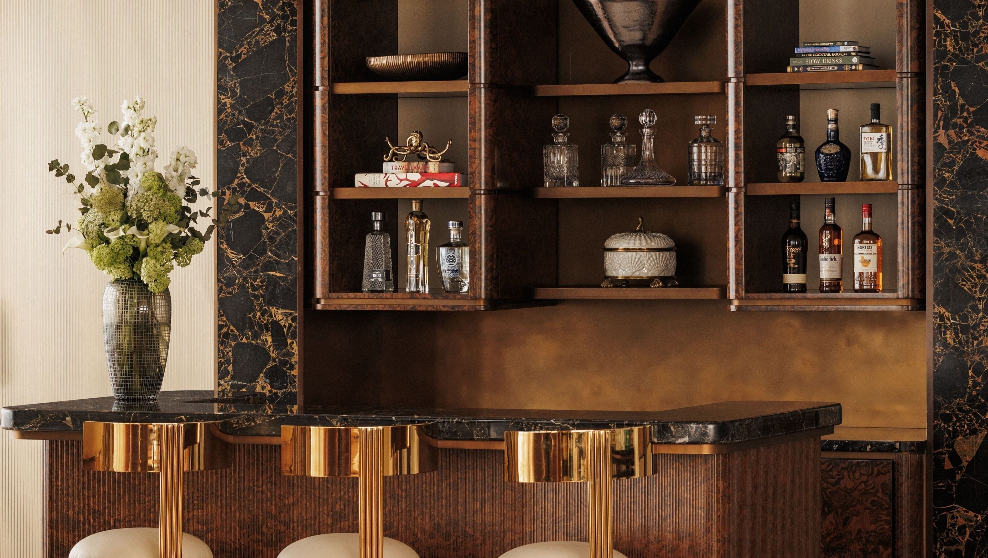 A bar area with a marble countertop, gold accents, and shelves with liquor bottles and decorative items.