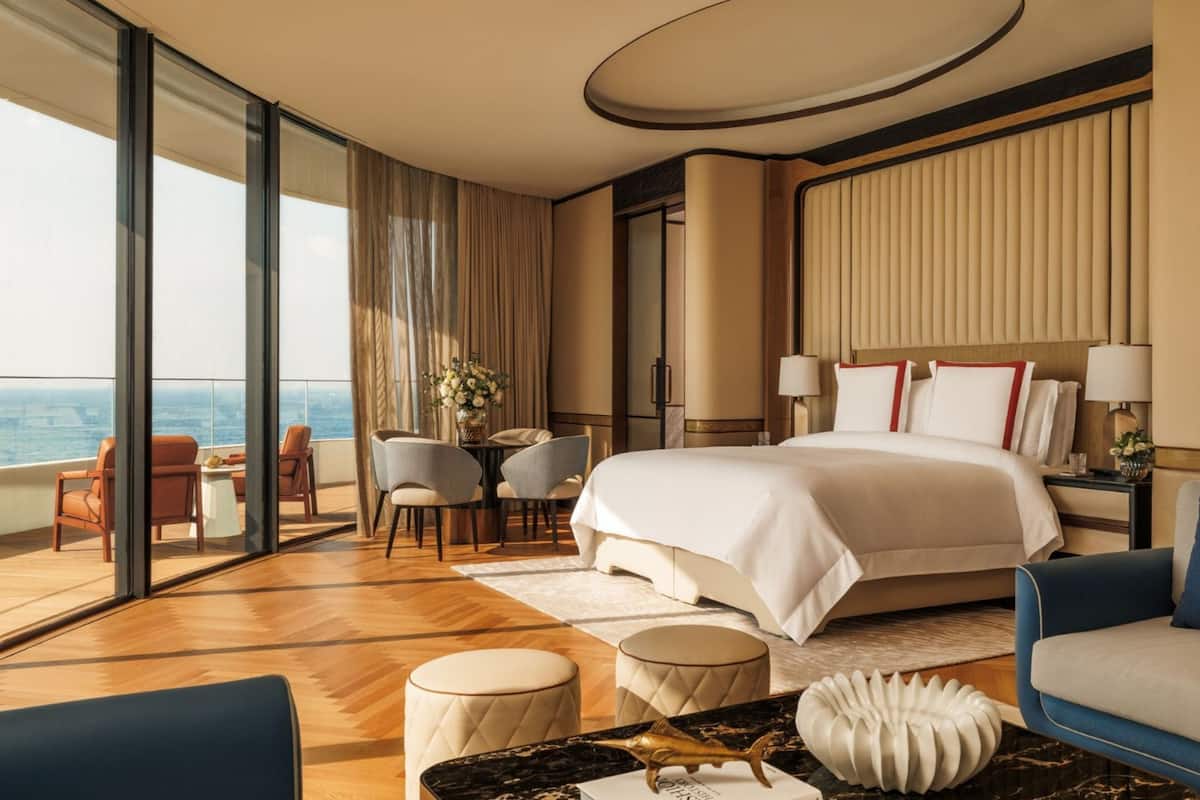 A modern hotel room with a large bed, a seating area with a table, and a view of the ocean.