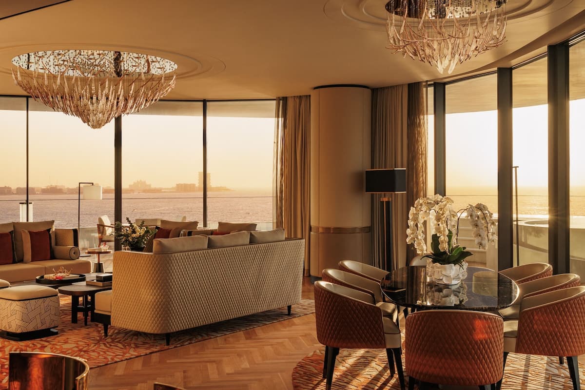 A spacious living area with a large sofa, a dining table with chairs, and a view of the sea.