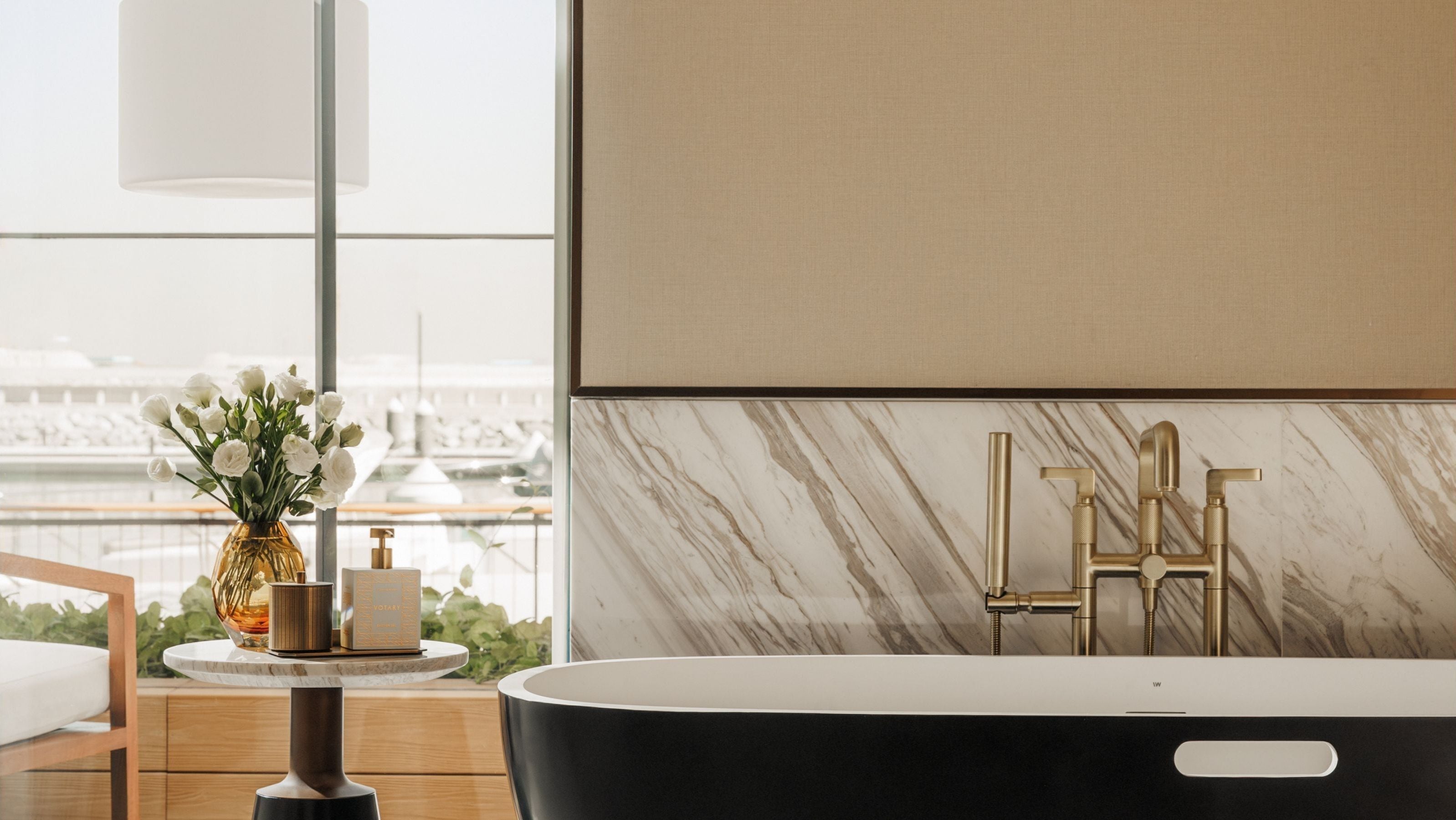 Ein modernes Badezimmer mit einer freistehenden Badewanne, einer Marmor-Spritzschutzwand und Blick auf eine Marina durch große Fenster.