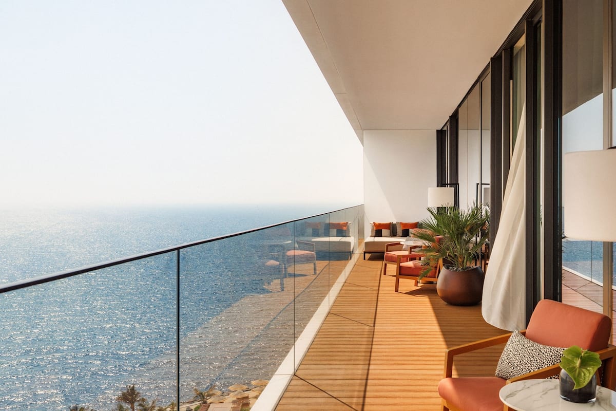 A modern balcony with a wooden floor, a sofa, a chair, a table, and a potted plant.