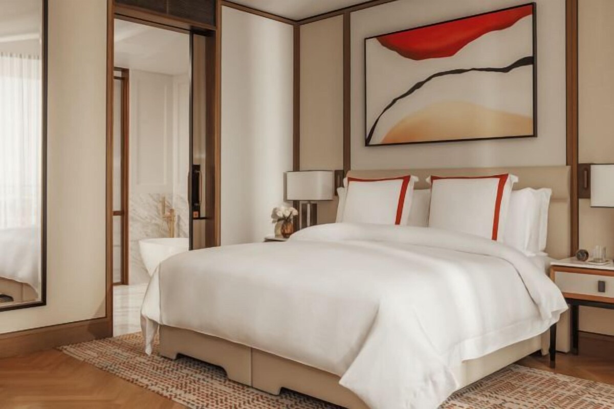A hotel room with a large bed, bedside tables, a mirror, and a painting on the wall.