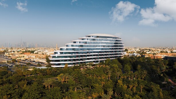 A modern multi-story hotel with a curved facade, surrounded by dense greenery and a cityscape in the background. - Jumeirah Residences Marsa Al Arab (Dubai)