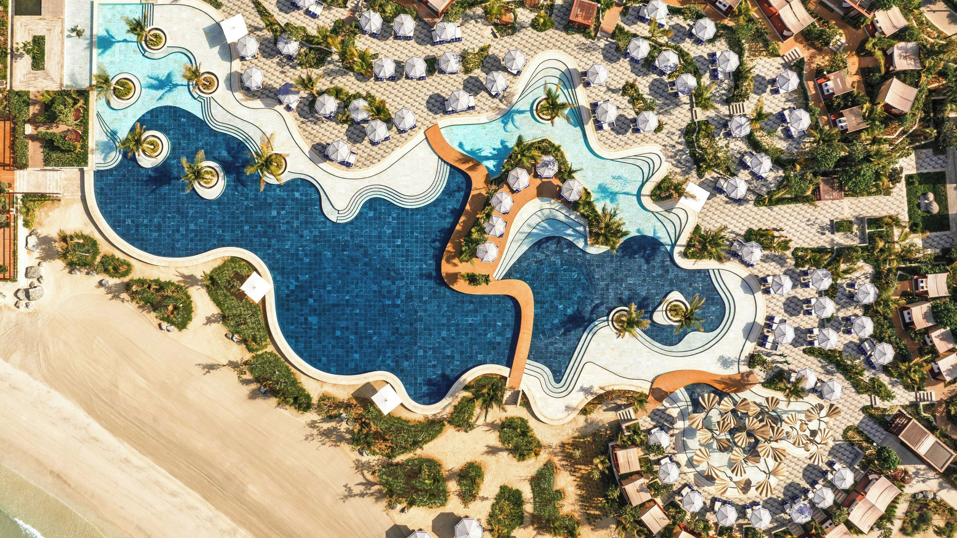 An aerial view of a resort with multiple swimming pools, sun loungers, and umbrellas.