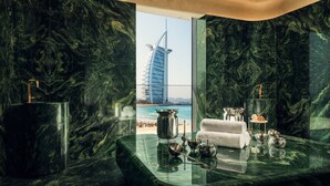 A luxurious bathroom with a view of the Burj Al Arab hotel. It features a marble vanity, a large mirror, and a glass table with toiletries. - Jumeirah Residences Marsa Al Arab (Dubai)