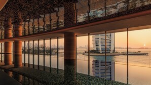 A modern interior with a reflective floor, large windows, and a view of a city skyline and water body. - Jumeirah Residences Marsa Al Arab (Dubai)