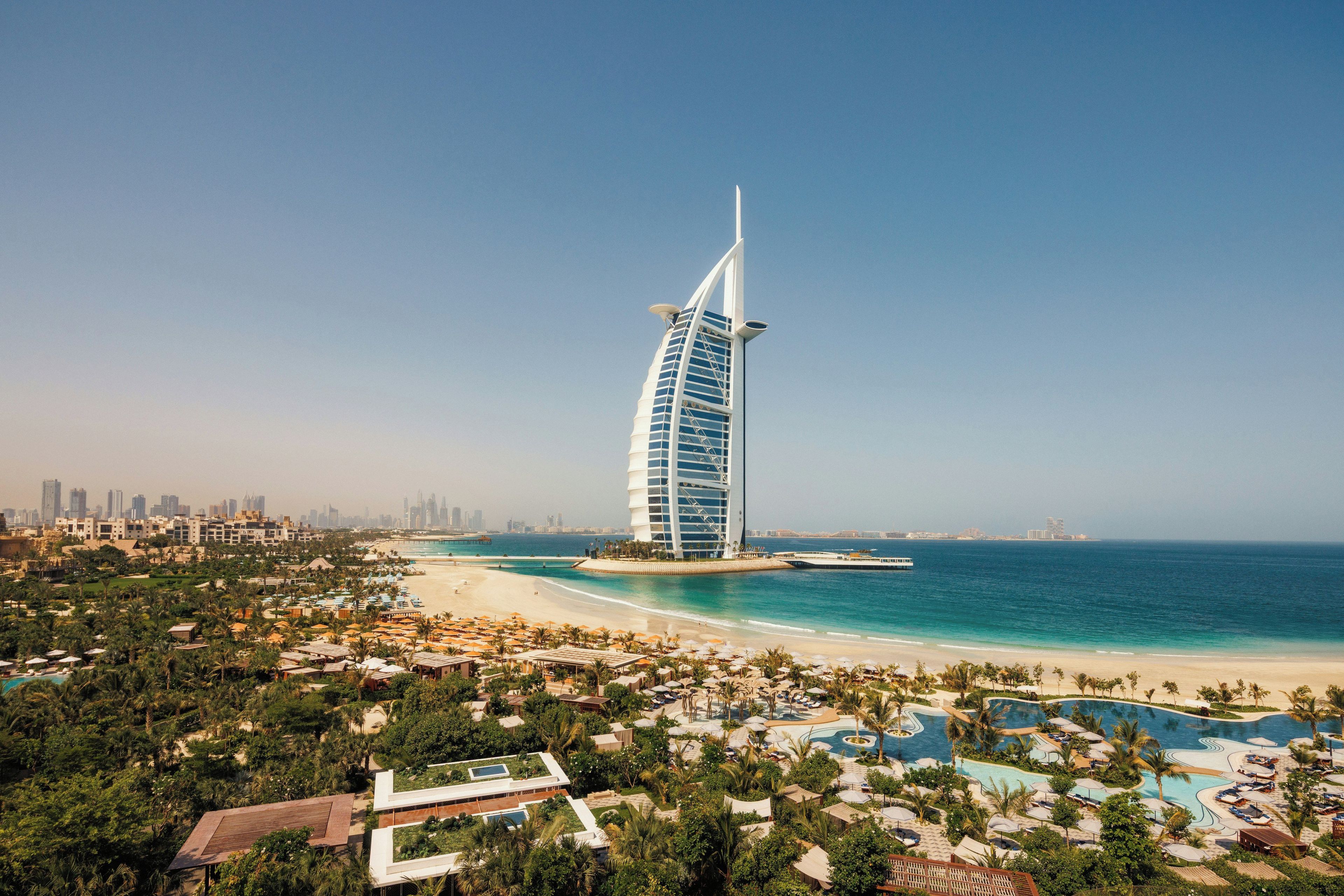 A coastal resort with a prominent sail-shaped hotel, a beach, and a pool area.