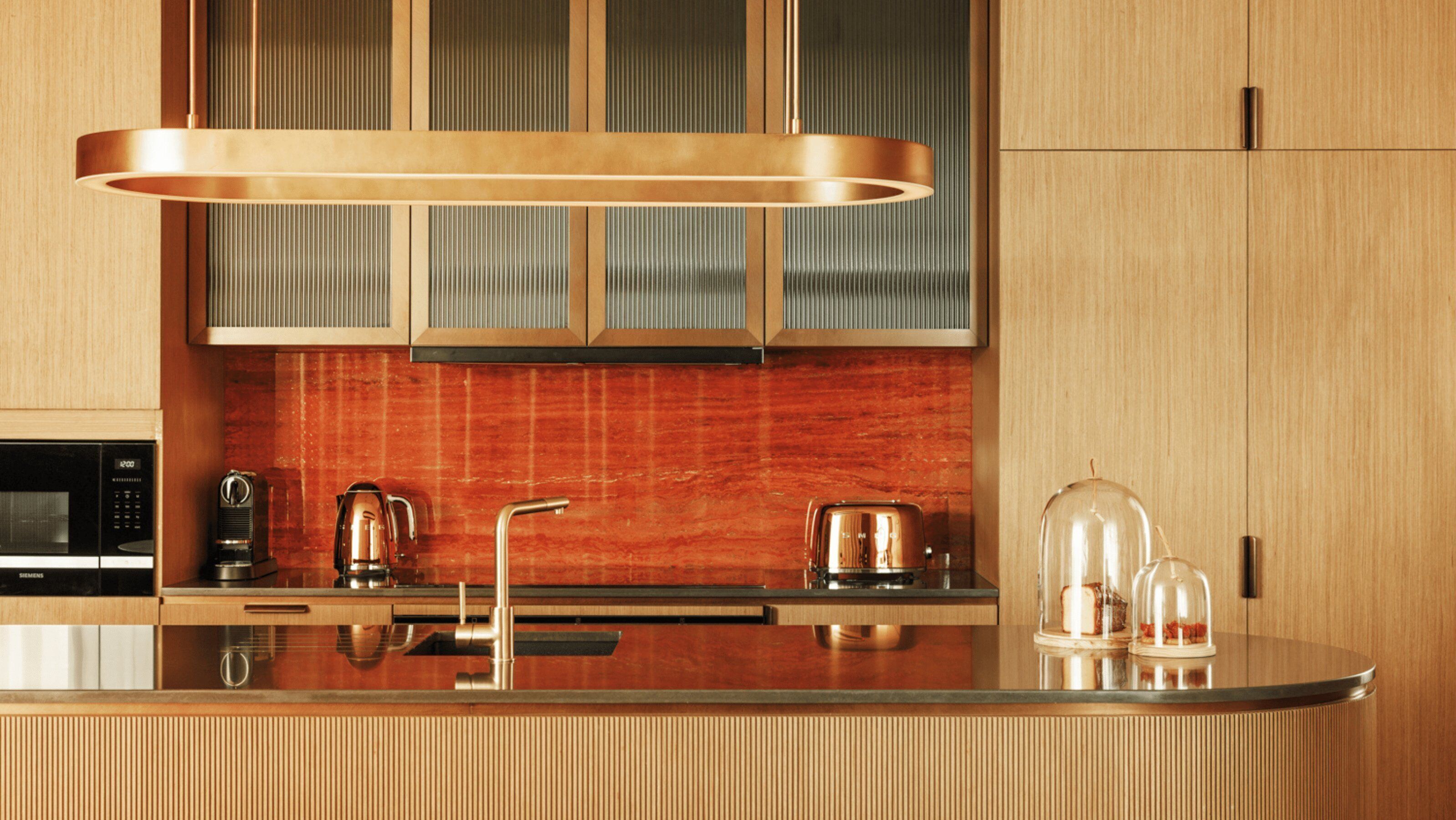 A modern kitchen with a stainless steel countertop, a built-in oven, a coffee machine, and a glass-enclosed display case.