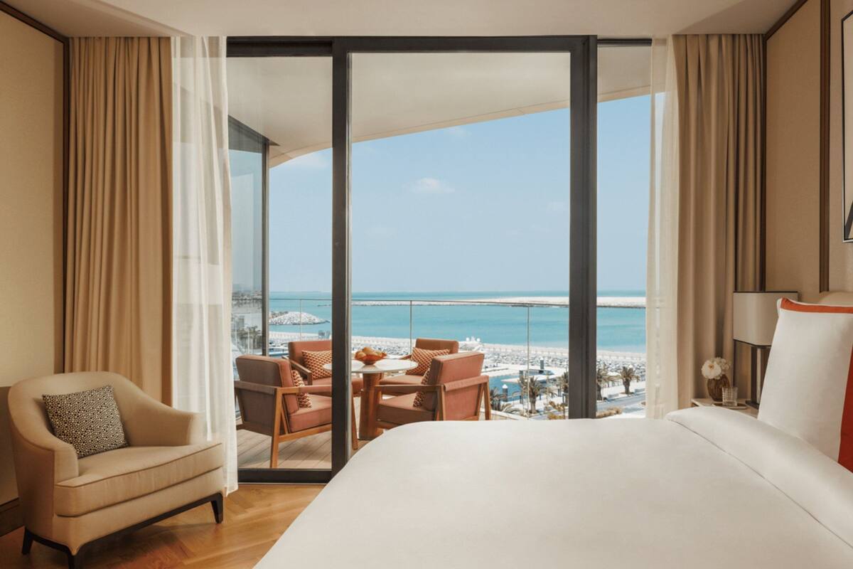 A hotel room with a large bed, a chair, a table, and a view of the beach and ocean.