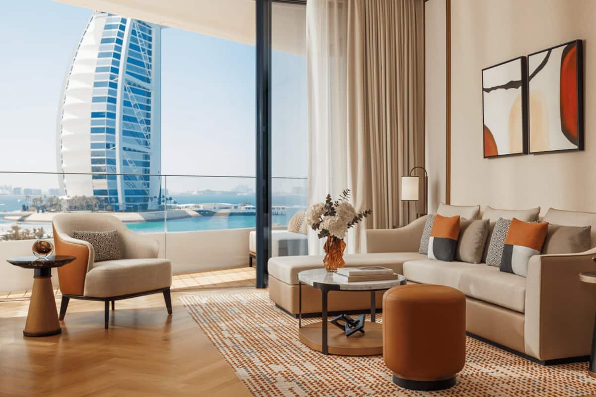A modern living room with a sofa, armchair, and coffee table, a view of a city skyline, and a decorative vase with flowers.